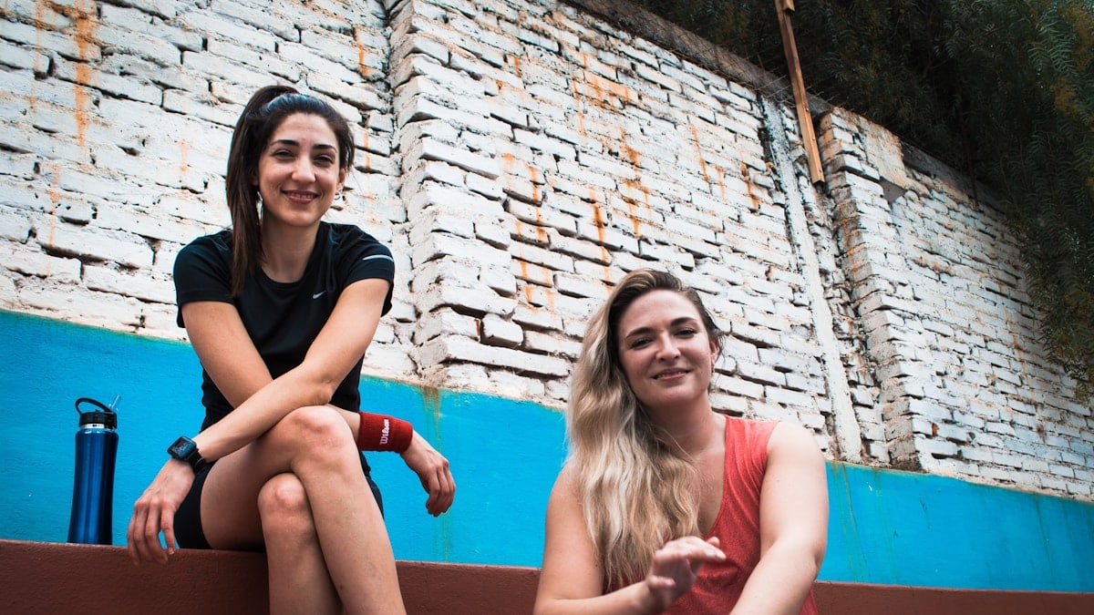 two women sitting on a wall with a brick wall behind them